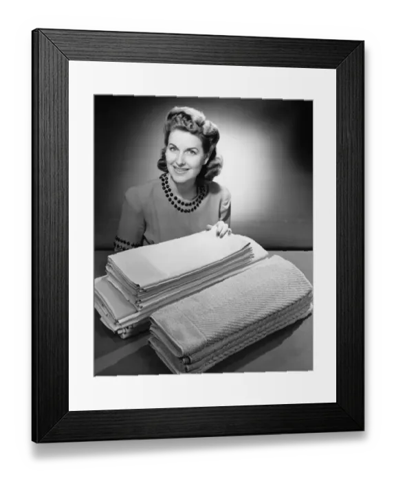 Framed Print : Woman sitting at pile of ironed linen and towels (B&W), portrait Framed Print : Woman sitting at pile of ironed linen and towels (B&W), portrait