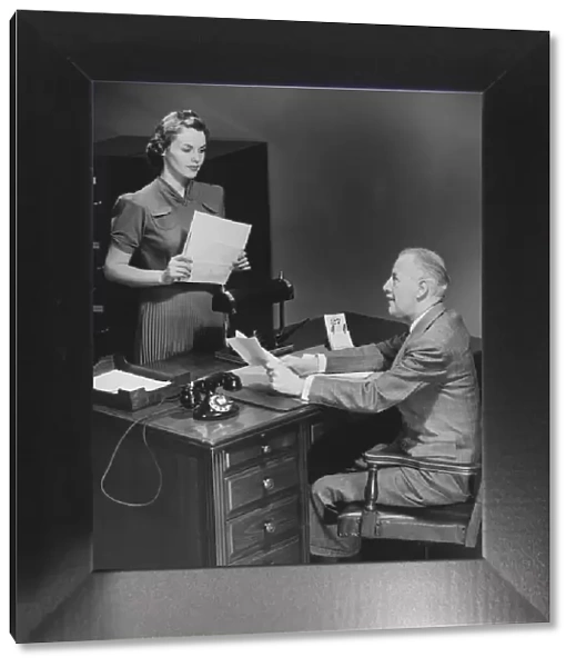 Businessman sitting at desk talking to secretary (B&W)