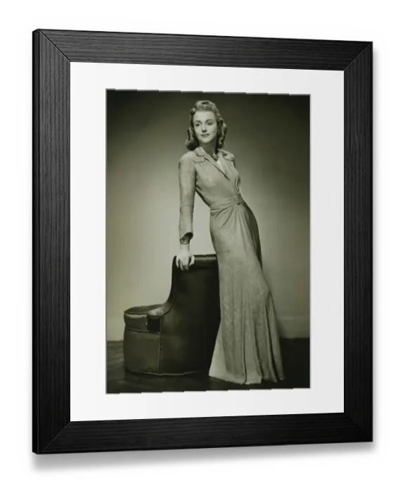 Framed Print : Young woman in evening dress leaning against chair, (B&W) Framed Print : Young woman in evening dress leaning against chair, (B&W)