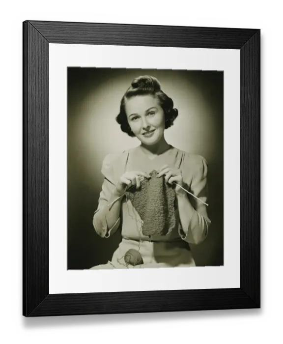 Framed Print : Young woman knitting in studio, (B&W), portrait
