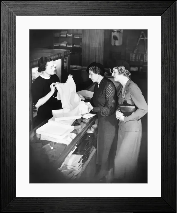 Framed Print : Sales clerk presenting lingerie to clients (B&W) Framed Print : Sales clerk presenting lingerie to clients (B&W)