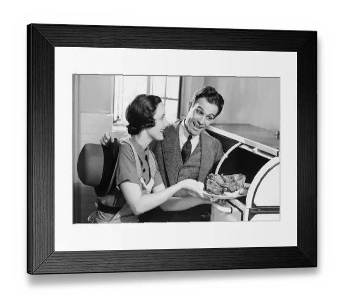 Framed Print : Couple in kitchen, wife taking roast from oven, (B&W) Framed Print : Couple in kitchen, wife taking roast from oven, (B&W)