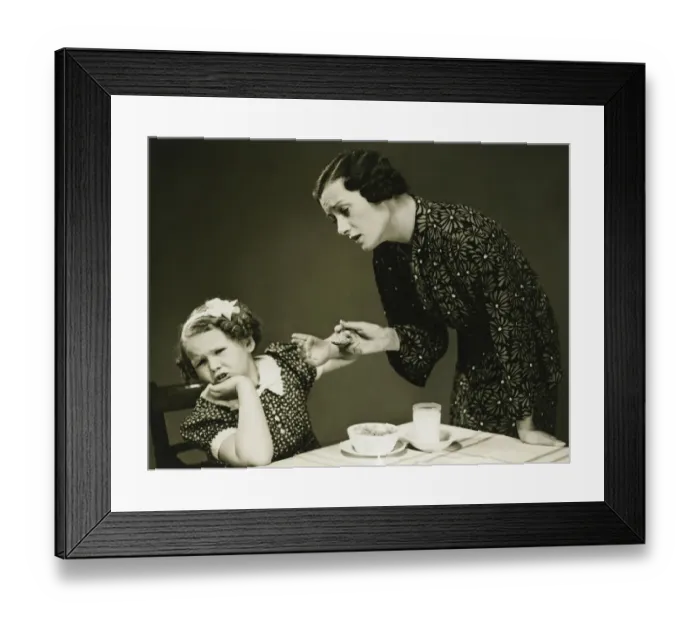 Framed Print : Mother trying to make daughter (4-5) finish food at table, (B&W) Framed Print : Mother trying to make daughter (4-5) finish food at table, (B&W)