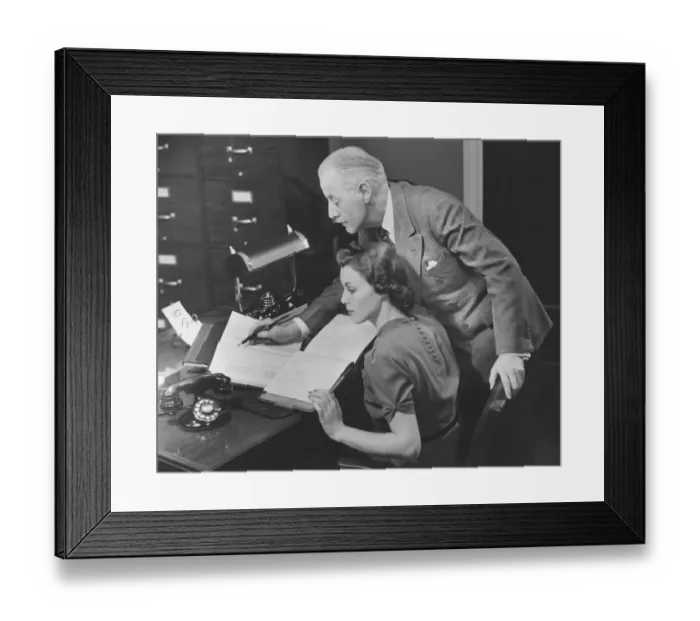 Framed Print : Mature businessman overseeing secretarys work, (B&W) Framed Print : Mature businessman overseeing secretarys work, (B&W)