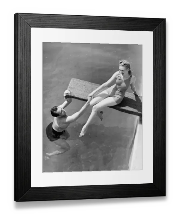 Framed Print : Woman sitting on diving board, man grasping her hand (B&W), elevated view Framed Print : Woman sitting on diving board, man grasping her hand (B&W), elevated view
