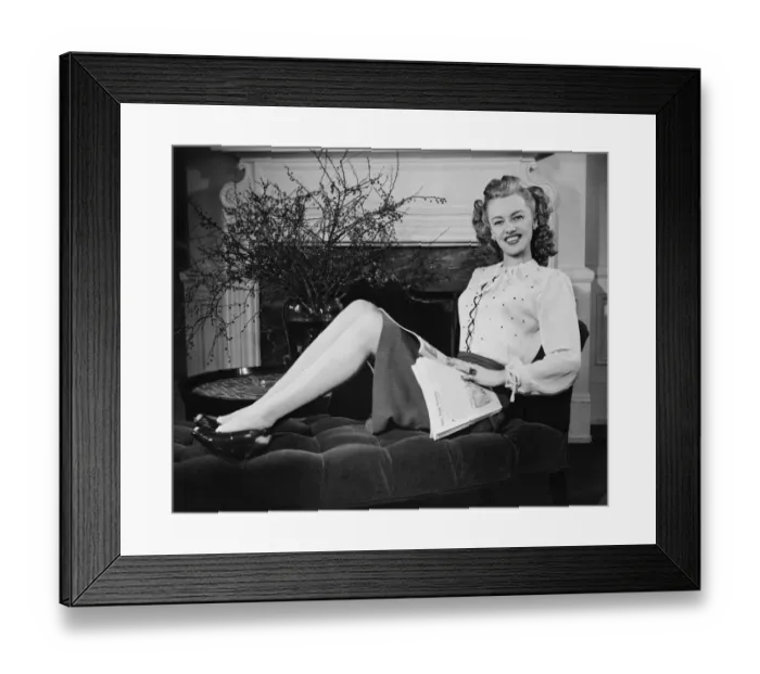 Framed Print : Woman with magazine sitting on chaise longue in living room, (B&W), portrait Framed Print : Woman with magazine sitting on chaise longue in living room, (B&W), portrait