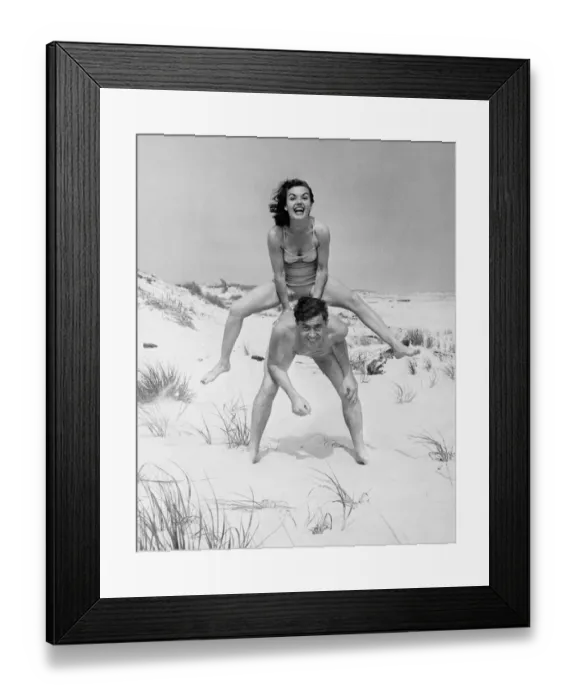 Framed Print : Young couple on beach, woman leap-frogging man, (B&W), portrait Framed Print : Young couple on beach, woman leap-frogging man, (B&W), portrait