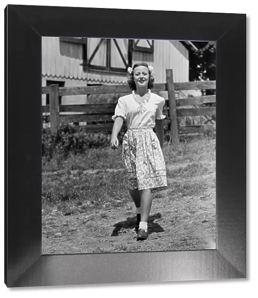 Young woman walking on dirt road by farmhouse, (B&W)