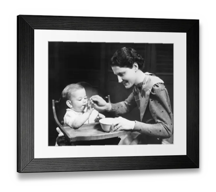 Framed Print : Woman feeding baby (6-9 months) sitting on high chair (B&W) Framed Print : Woman feeding baby (6-9 months) sitting on high chair (B&W)
