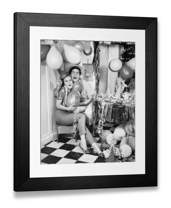 Framed Print : Smiling couple sitting in kitchen amongst party preparations, (B&W), portrait Framed Print : Smiling couple sitting in kitchen amongst party preparations, (B&W), portrait