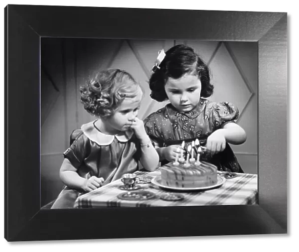 Two girls (4-5) standing at table with birthday cake (B&W)