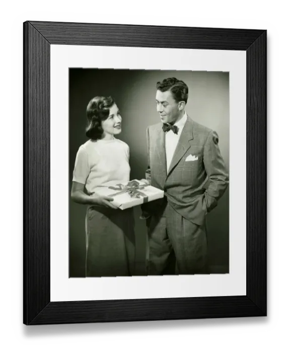 Framed Print : Couple standing in studio, woman holding present, (B&W) Framed Print : Couple standing in studio, woman holding present, (B&W)