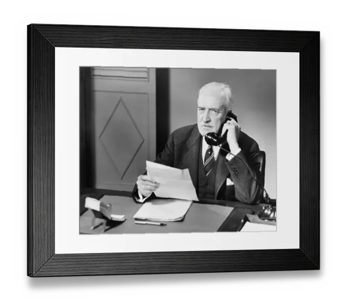 Framed Print : Senior talking on phone at desk in office (B&W) Framed Print : Senior talking on phone at desk in office (B&W)