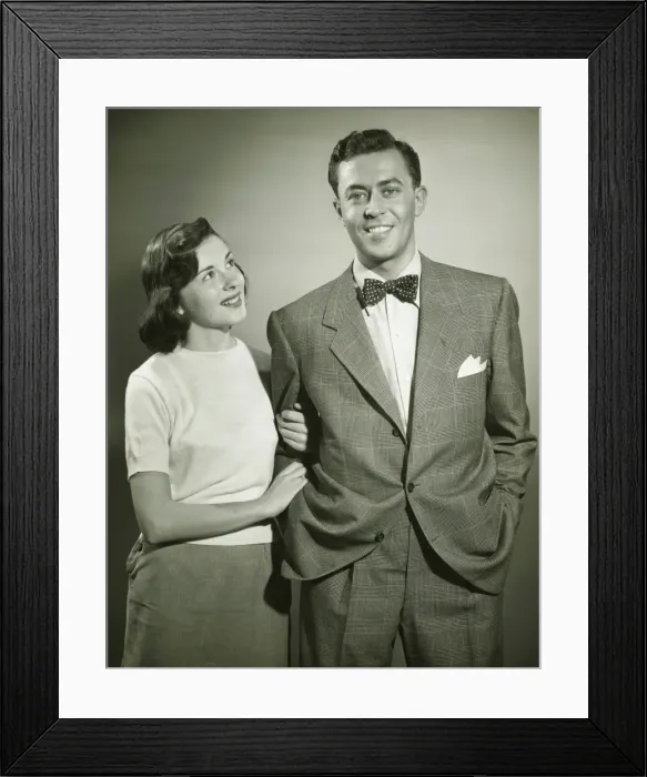 Framed Print : Young couple arm in arm in studio, woman looking at man, smiling, (B&W) Framed Print : Young couple arm in arm in studio, woman looking at man, smiling, (B&W)