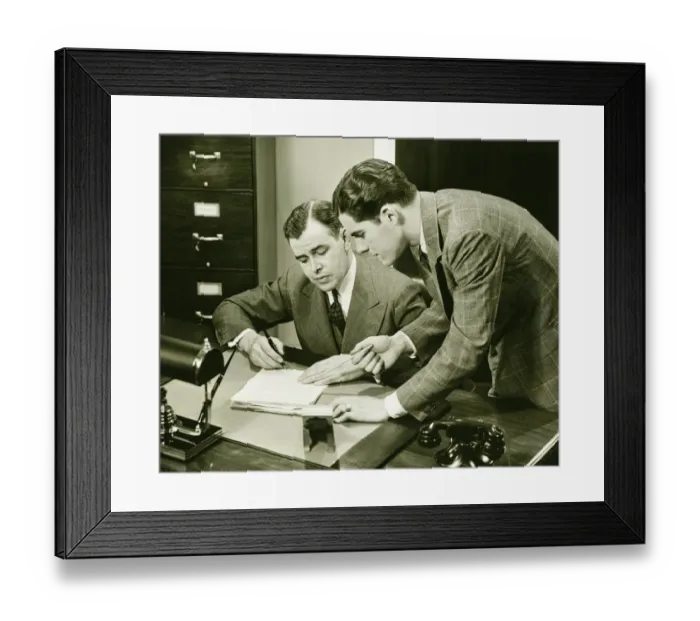Framed Print : Two young businessmen talking at small desk, (B&W) Framed Print : Two young businessmen talking at small desk, (B&W)
