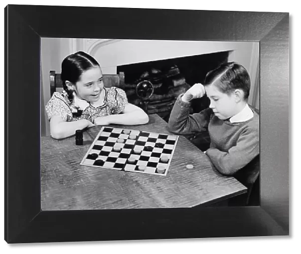 Boy and girl (8-9) playing checkers (B&W), elevated view
