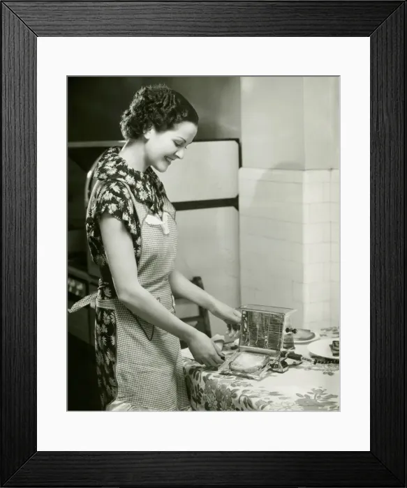 Framed Print : Young woman making slice of toast, (B&W), portrait Framed Print : Young woman making slice of toast, (B&W), portrait