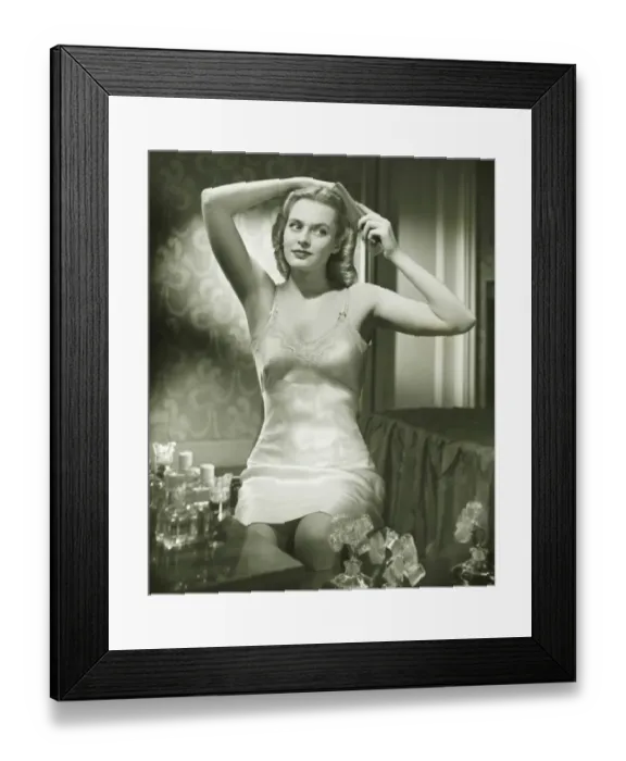 Framed Print : Woman in underskirt brushing hair in bedroom, (B&W), portrait