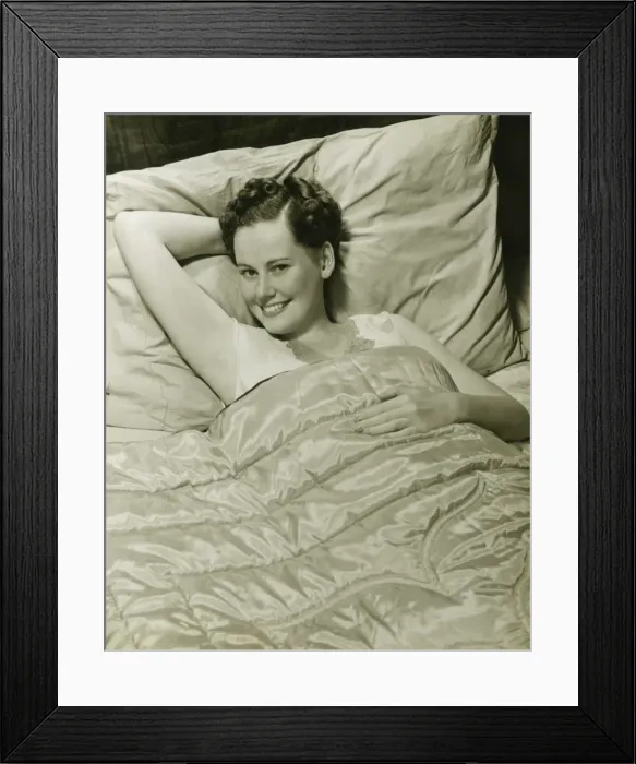 Framed Print : Young woman lying in bed, smiling, (B&W), portrait Framed Print : Young woman lying in bed, smiling, (B&W), portrait