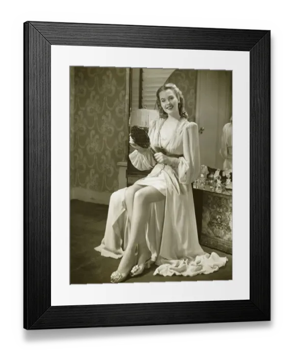 Framed Print : Young woman holding mirror, sitting at dresser, (B&W) Framed Print : Young woman holding mirror, sitting at dresser, (B&W)