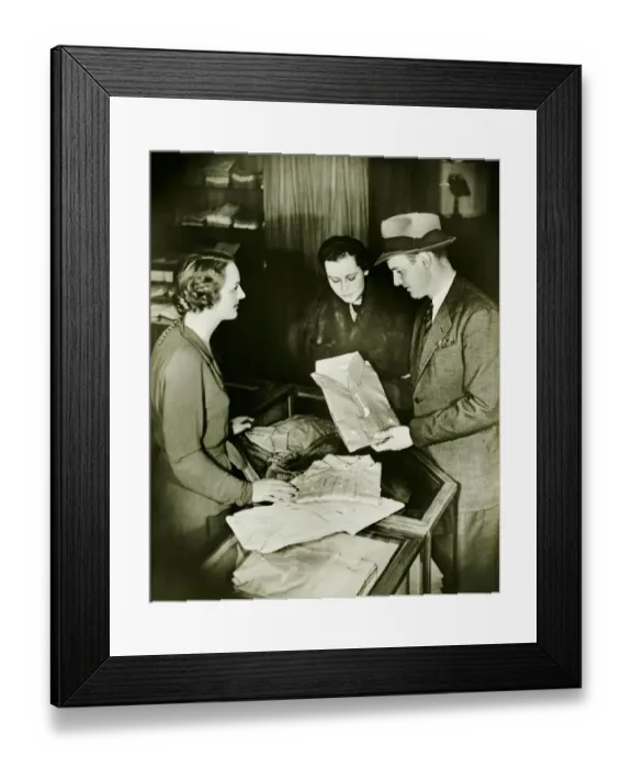 Framed Print : Young couple buying shirt, standing at counter, (B&W) Framed Print : Young couple buying shirt, standing at counter, (B&W)
