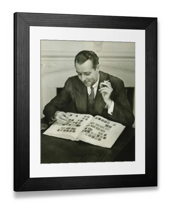 Framed Print : Businessman sitting at small table, with stamp album, (B&W) Framed Print : Businessman sitting at small table, with stamp album, (B&W)