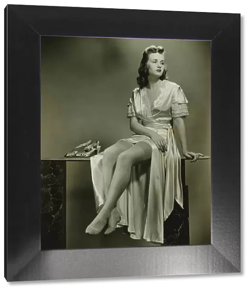 Young woman in elegant dressing gown sitting in studio, (B&W)
