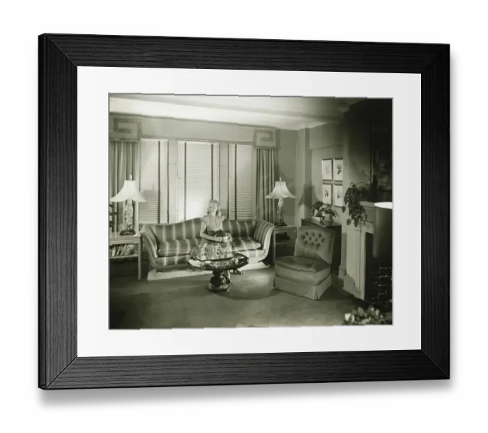 Framed Print : Woman sitting on sofa in stylish living room, (B&W) Framed Print : Woman sitting on sofa in stylish living room, (B&W)