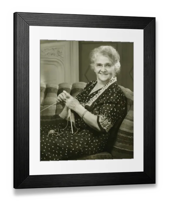 Framed Print : Senior woman knitting in living room, (B&W), portrait
