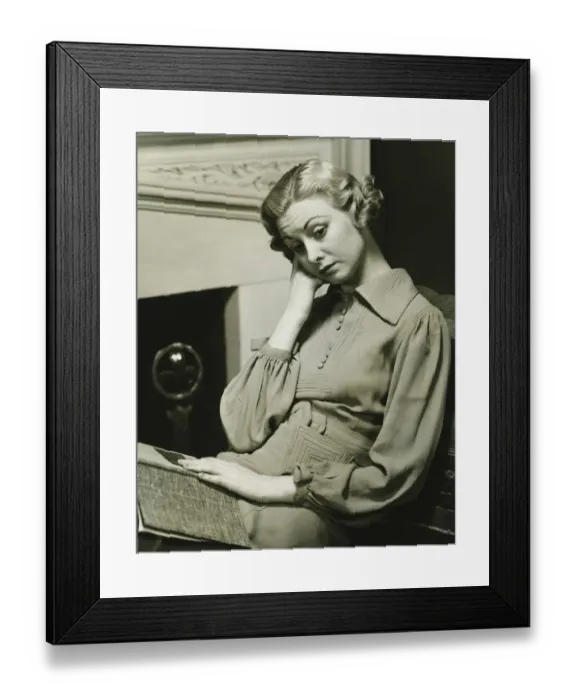 Framed Print : Pensive woman sitting by fireplace with book on laps, (B&W) Framed Print : Pensive woman sitting by fireplace with book on laps, (B&W)