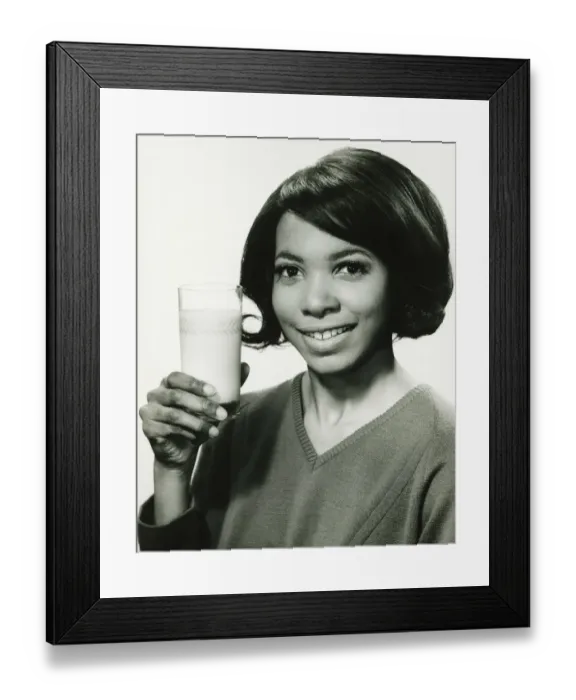 Framed Print : Young woman holding glass of milk in studio, smiling, (B&W), portrait