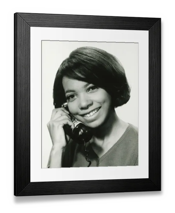 Framed Print : Young woman using phone in studio, smiling, (B&W), portrait Framed Print : Young woman using phone in studio, smiling, (B&W), portrait