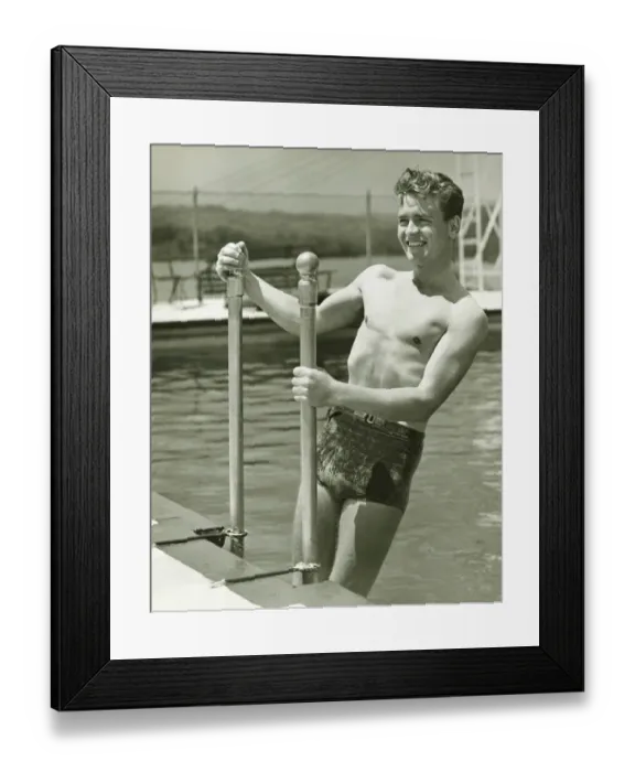 Framed Print : Young man standing on pool ladder, (B&W) Framed Print : Young man standing on pool ladder, (B&W)