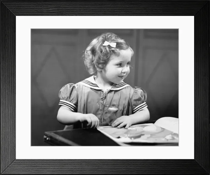 Framed Print : Young girl (4-5) at table reading book, (B&W) Framed Print : Young girl (4-5) at table reading book, (B&W)