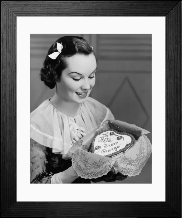 Framed Print : Young woman holding heart-shaped cake, (B&W) Framed Print : Young woman holding heart-shaped cake, (B&W)