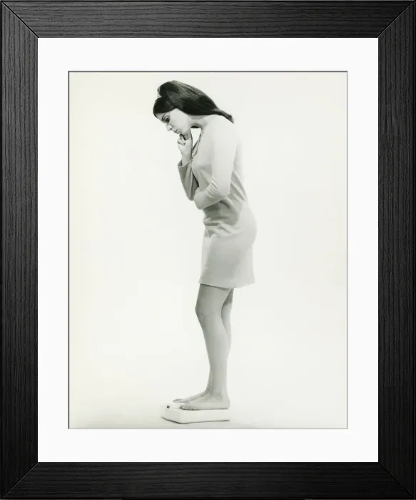 Framed Print : Woman standing on scale in studio, (B&W) Framed Print : Woman standing on scale in studio, (B&W)