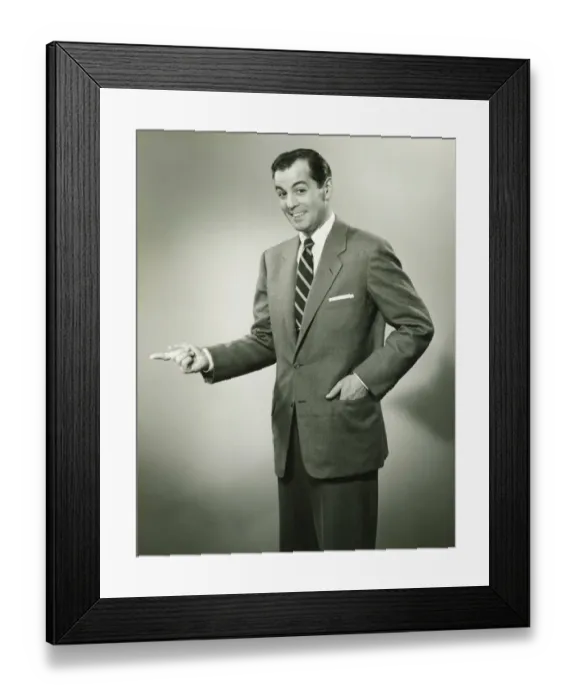 Framed Print : Businessman pointing sideways in studio, smiling, (B&W), portrait Framed Print : Businessman pointing sideways in studio, smiling, (B&W), portrait