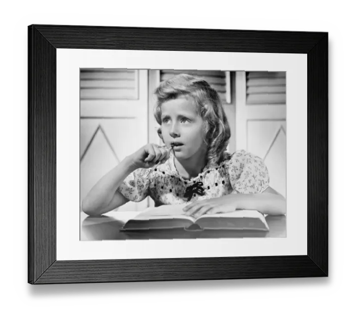 Framed Print : Girl (8-9) sitting at table, holding pencil in mouth, (B&W), close-up Framed Print : Girl (8-9) sitting at table, holding pencil in mouth, (B&W), close-up