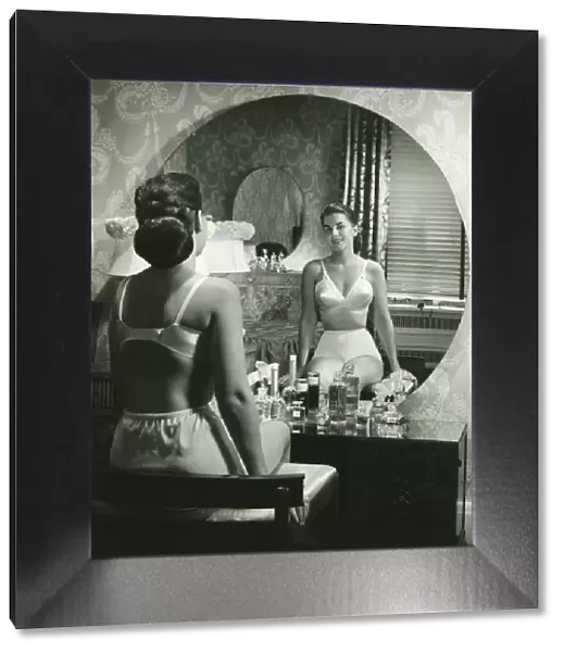 Woman in underwear sitting in front of vanity table, (B&W), rear view