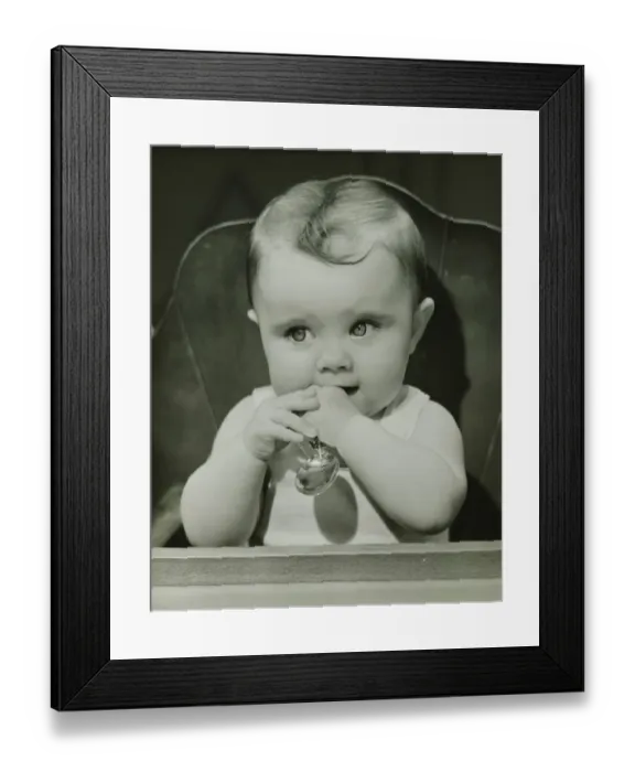 Framed Print : Baby (6-9 months) sitting in high chair, holding spoon, (B&W), portrait Framed Print : Baby (6-9 months) sitting in high chair, holding spoon, (B&W), portrait
