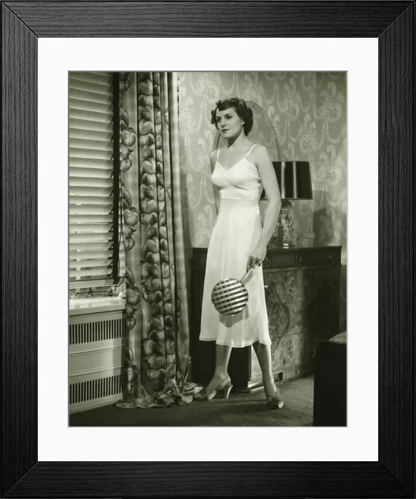 Framed Print : Young woman standing in living room, holding mirror, (B&W) Framed Print : Young woman standing in living room, holding mirror, (B&W)