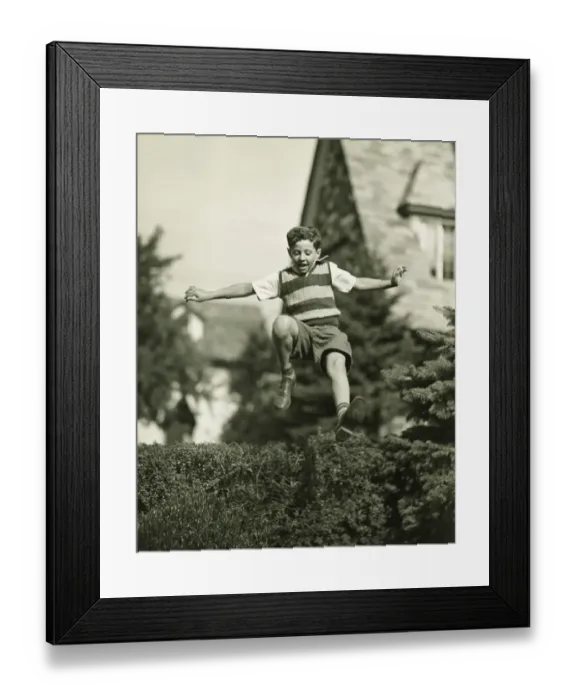 Framed Print : Teenage boy (13-14) leaping over hedge, (B&W), low angle view Framed Print : Teenage boy (13-14) leaping over hedge, (B&W), low angle view