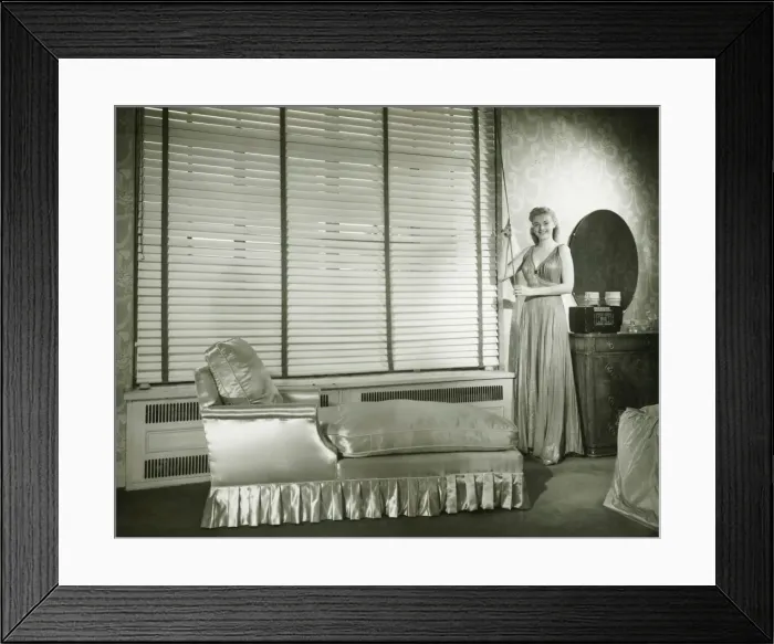 Framed Print : Young woman standing in living room, opening Venetian blinds, (B&W) Framed Print : Young woman standing in living room, opening Venetian blinds, (B&W)