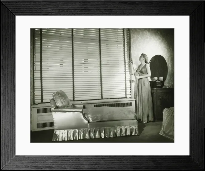 Framed Print : Woman adjusting window blind in living room, (B&W) Framed Print : Woman adjusting window blind in living room, (B&W)