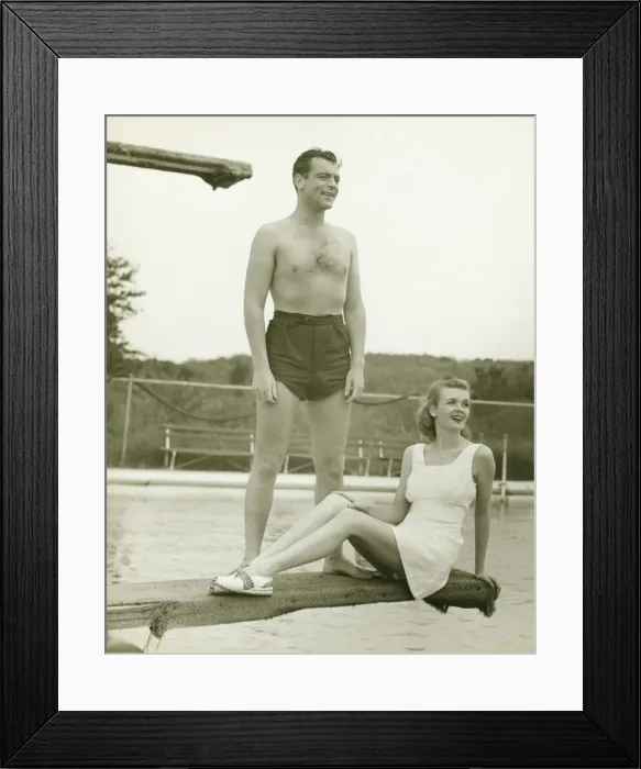 Framed Print : Young couple on springboard, man standing, woman sitting, (B&W) Framed Print : Young couple on springboard, man standing, woman sitting, (B&W)