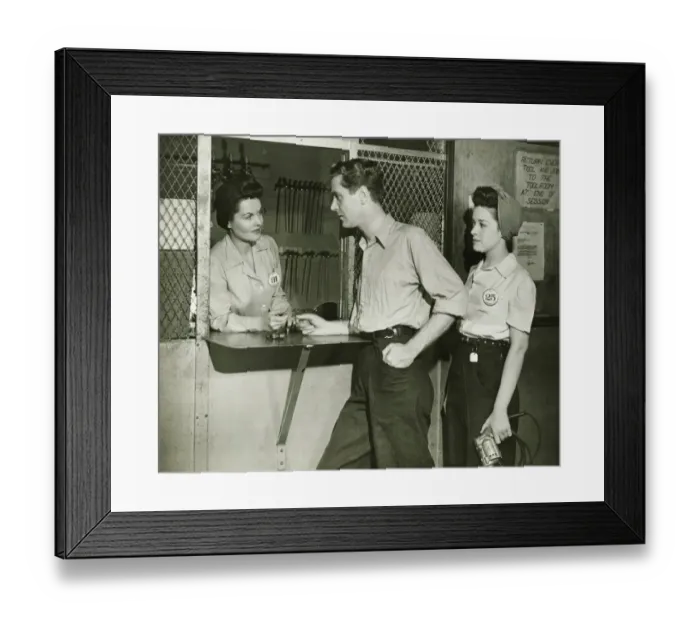 Framed Print : Young man and woman returning tools at tool room window, (B&W) Framed Print : Young man and woman returning tools at tool room window, (B&W)