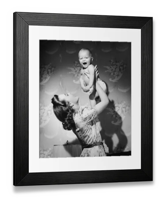 Framed Print : Woman lifting up baby (6-9 months) at home, (B&W)