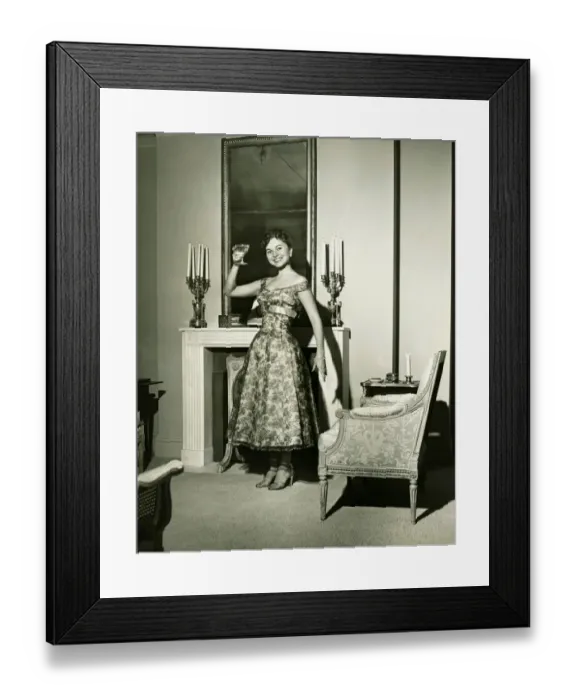 Framed Print : Woman in evening gown toasting by fireplace, (B&W), portrait Framed Print : Woman in evening gown toasting by fireplace, (B&W), portrait