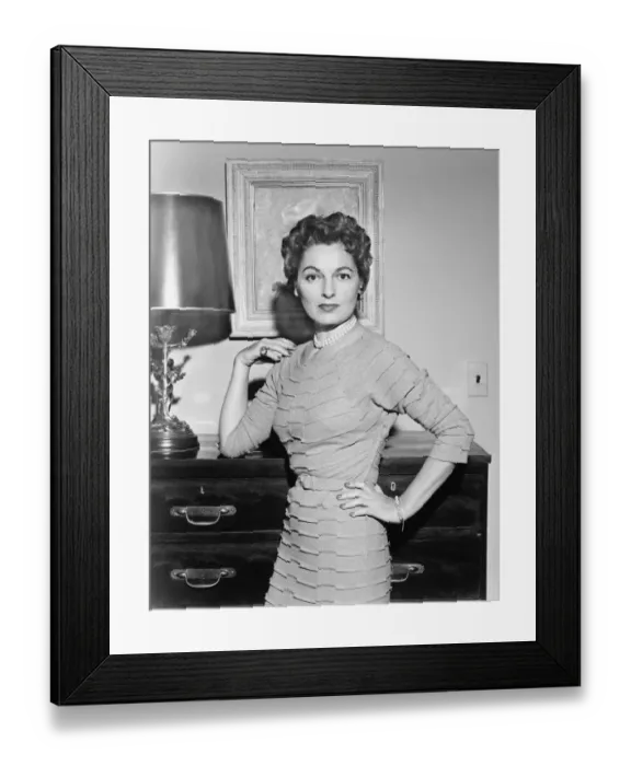 Framed Print : Woman standing in living room with hand on cabinet, (B&W)
