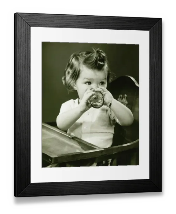 Framed Print : Girl (2-3) sitting in high chair, drinking water from glass, (B&W) Framed Print : Girl (2-3) sitting in high chair, drinking water from glass, (B&W)